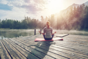 Woman sitting on yoga mat on a pier near a lake